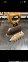 Photo showing the antique clothes iron with wooden handle and the separate iron slug placed in front of it on a work surface.
