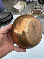 Copper dish held in hand showing the hammered texture and patina on the side and base.