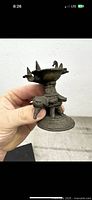Side view of antique bronze oil lamp showing detailed elephant base and lamp bowl with three spouts.