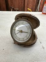 Front view of the antique Hengis mechanical pocket clock in its partially open leather case on a white surface, showing clear clock face with numeric markers and gold hands