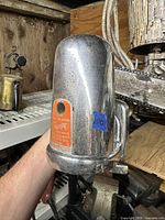 Chrome Art Deco powdered soap dispenser with orange label and mounting hardware seen on wooden shelf.