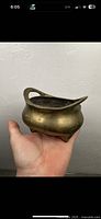 Photo of front and side view of bronze censer showing rounded body, curved handle, and three legs