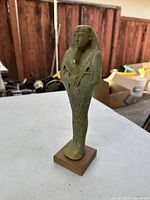 Full view of the large stone-like Ushabti figurine standing on a wooden base, showing front and side detailing.
