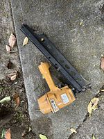 Full view of the yellow Bostitch framing nailer lying on a concrete surface with leaves around.