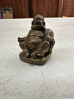 Small brass Buddha statue placed on a table with wood background, showing full figure and base.