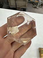 Photo showing clear hexagon-shaped quartz held in hand, displaying faceted edges and transparent surface with internal natural crack.