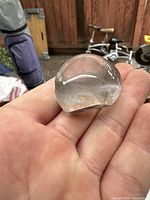 Hand holding small polished clear quartz ball with visible internal inclusions and natural fractures