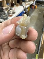 Close-up photo showing side profile of the small carved agate wolf statue held between thumb and index finger, highlighting texture and translucency of agate stone.
