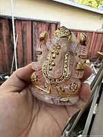 Front view of carved pink rose quartz Ganesha statue showing gold and colored enamel details, held in hand.