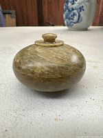 Photo of the closed stone container showing its rounded shape and knob lid on a white surface.