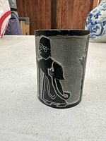 Carved stone cylindrical paperweight with an Egyptian styled female figure engraved in black outlines.