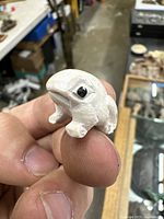 Photo showing the front and side of the small carved stone frog/toad netsuke held between fingers.