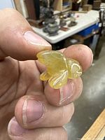 Photo showing the front and side detail of the small yellow carved frog netsuke, held between fingers for scale and detail visibility.