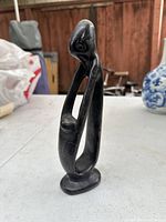 Full view of dark stone carved statue showing elongated mother figure holding child above hip.