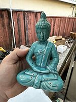 Front view of the blue turquoise glazed seated Buddha porcelain statue held in hand, showing wear marks.