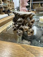 Angular front view showing the irregular hole pattern and natural stone texture of the soapstone display pedestal sitting on a glass surface with wooden framing around.