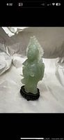 Carved Guanyin figure showing full front with light green jade serpentine material on green wooden base