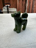 Image of the green nephrite jade dog figurine on a light-colored surface, showing side profile and tail curl.