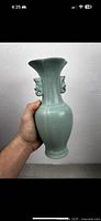 Vase held upright showing overall shape, glaze color, and double ear handles.