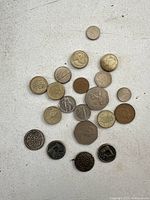 Top view of a mixed assortment of coins varying in size, metal, and condition scattered on a white surface.