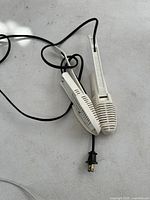 Pair of white electric boot warmers with a black power cord and plug, showing the full length of the warmers and their vented design on a white surface.