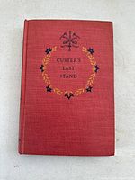 Front cover of red hardcover book titled 'Custer's Last Stand' with decorative wreath and arrows design in black and gold.