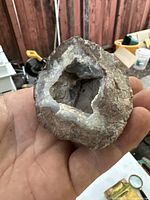Hand holding geode rock showing outer rough surface and inner crystalline cavity