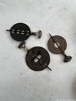 Three cast iron vintage stove top heating discs including two Griswold round discs with coil handles and one smaller round disc with coil handle placed on a light background.