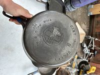 Bottom of Griswold cast iron skillet showing brand logo, size number 8, and casting marks including 'ERIE PA USA' and '704'. Surface shows some sulfur pitting.
