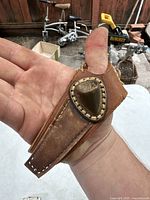 Front view of leather thumb sewing thimble with protective leather arm guard, metal thimble secured on thumb portion.