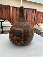 Front and side views of large hand carved African gourd vase with detailed geometric and animal designs.