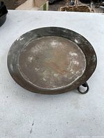 Top-down view of large antique copper pan showing flat surface and wide rim with metal loop handle visible on the rim.