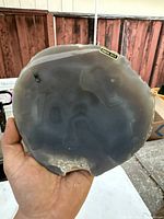 Front view of the hand-held agate slab showing the smooth, polished surface with natural gray and white banding patterns and a rough edge with crystals.