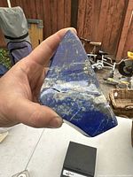 Photo of hand holding blue lapis lazuli stone with visible crack and metallic mineral inclusions