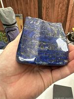 Polished deep blue lapis lazuli chunk with metallic veins held in hand to show size and detail.
