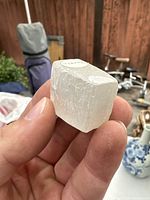 Photo of small white selenite specimen held between fingers showing cubic shape and crystalline texture.