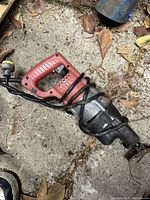 Full view of Milwaukee reciprocating saw lying on gravel surface with the cord wrapped around the handle.