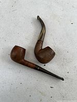 Both antique hurl pipes together on a flat surface showing their large burl wood bowls and dark stems in distinct shapes.