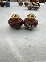 Pair of small round cloisonné salt and pepper shakers with brass tops and floral designs on red enamel bodies