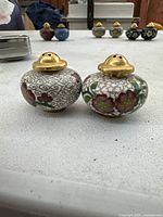 Pair of Chinese cloisonné salt and pepper shakers with decorative floral design and brass tops displayed on a white surface.