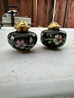 Front view of the pair of Chinese antique cloisonné salt and pepper shakers on a white surface with a reddish background.