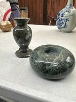 Pair of granite candleholders displayed on a white surface with background vases.