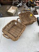 Two handwoven rectangular wicker baskets placed on a white table, showing their detailed weaving texture and handles.
