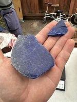 Large blue lapis lazuli stone sample resting on hand showing size and chipped edges with silver or pyrite veins visible.