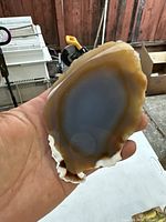 Palm-held polished agate stone showing brown and taupe banding with high reflection on surface.