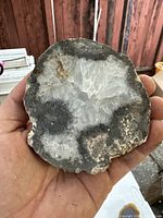 Top view of a polished crystal quartz geode held in hand, showing crystalline white and gray interior with rough exterior edge.