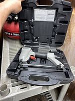 Porter Cable pneumatic nailer inside its black molded carrying case placed on a metal surface.