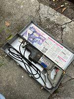 Photo of Tiger electric saw in worn metal case showing the tool and internal instructional label.