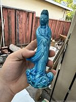 Front view of blue turquoise porcelain Guanyin figurine showing detailed face, hands, robe, and swirling base design held in hand.