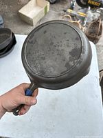 Bottom view of the BSR 7B cast iron skillet held by hand showing '7B' mark and surface wear.